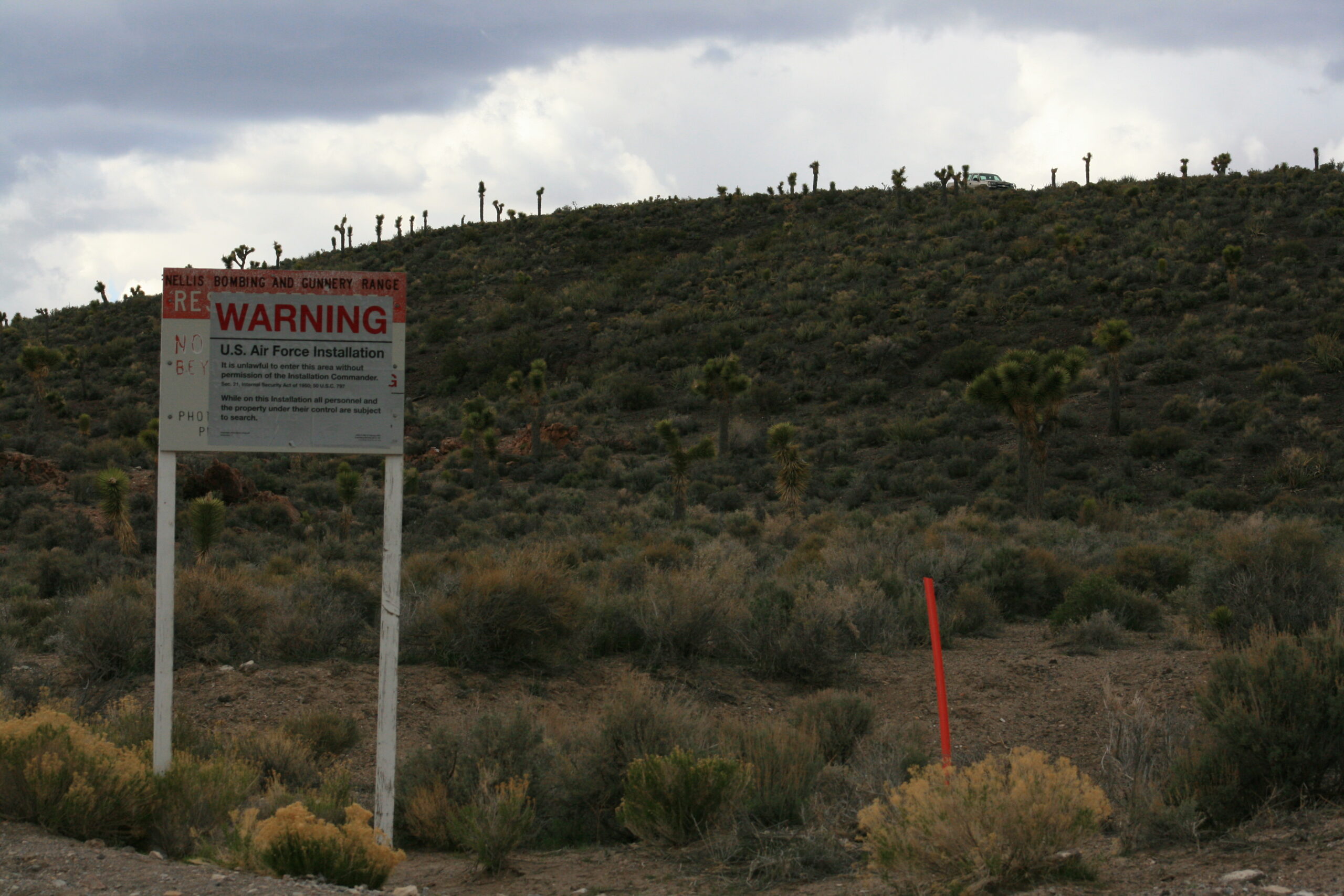 A sign warns trespassers at the boundary of Area 51 as security officers in a truck keep watch from a ridge.