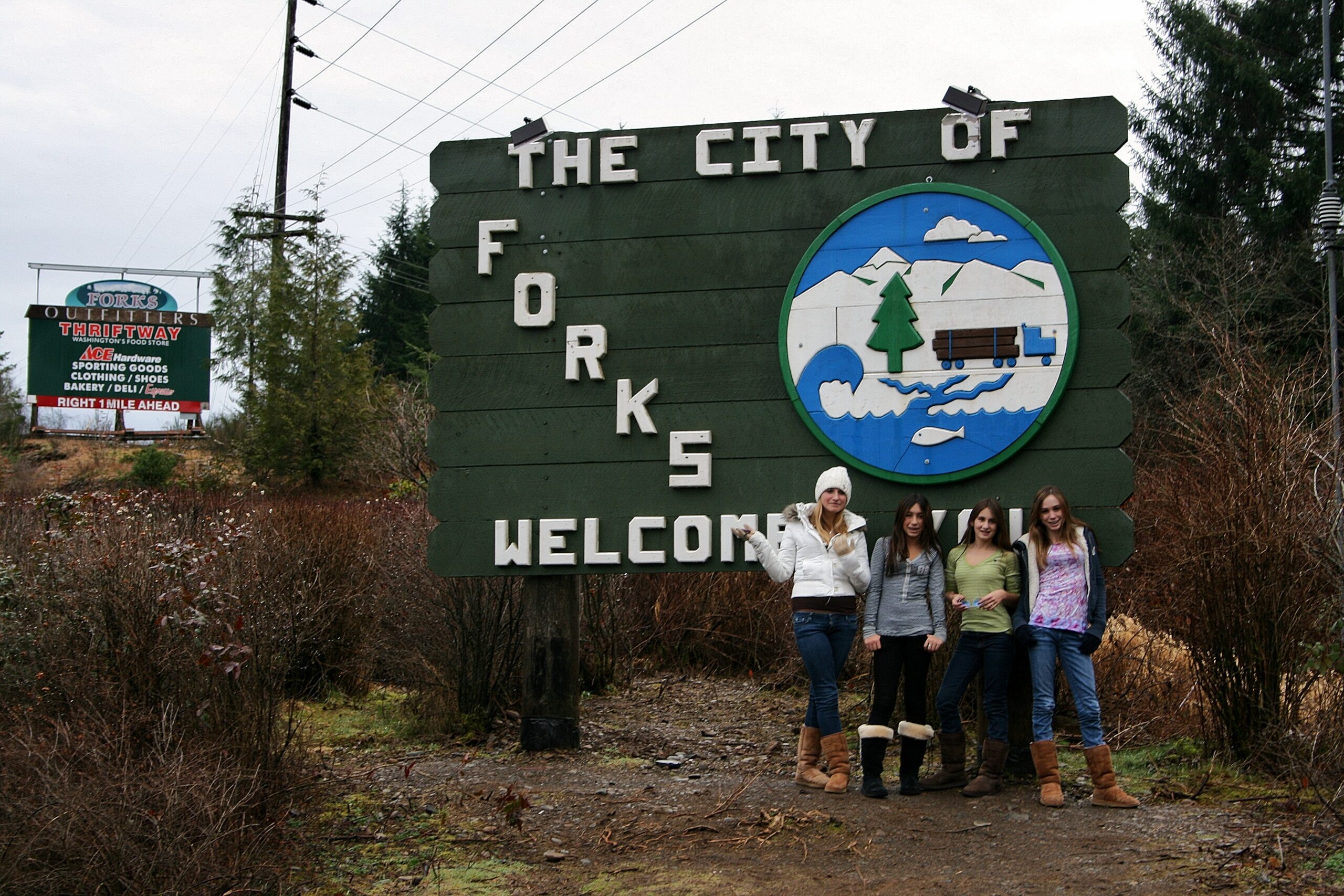 Tween Twilight fans stand in front of the Forks welcome sign.