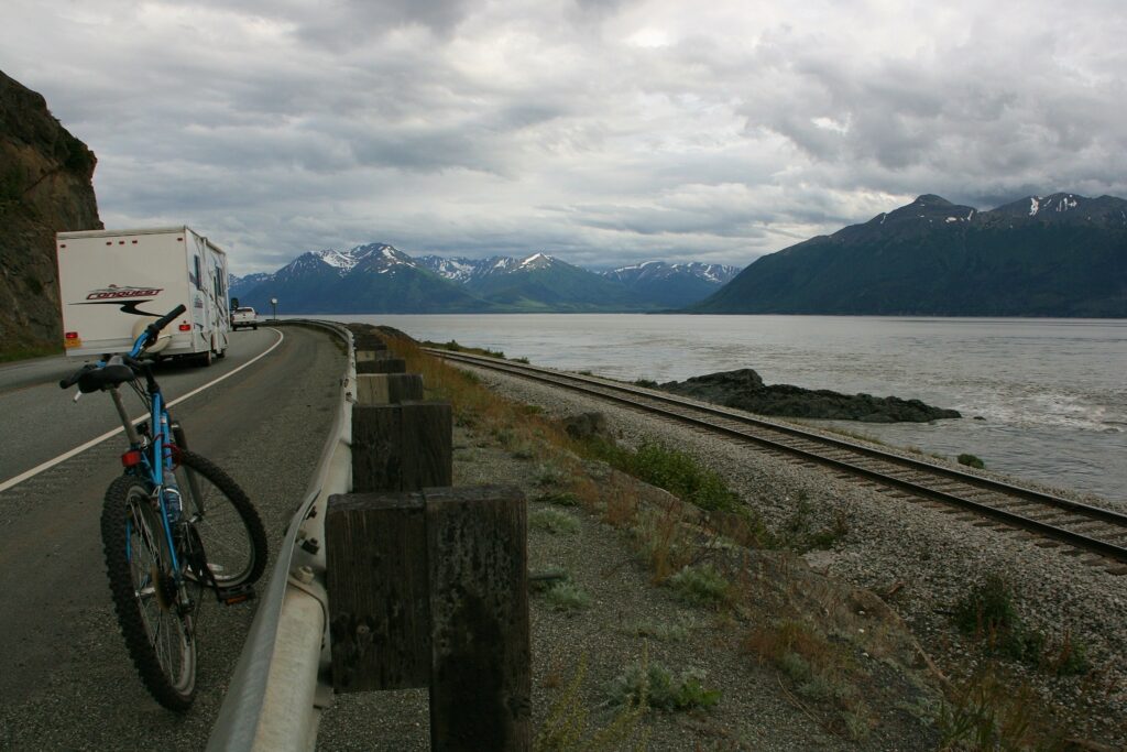 An RV passes a bicycle sitting on the Seward Highway near Alaska's Cook Inlet and Kenai Mountains.