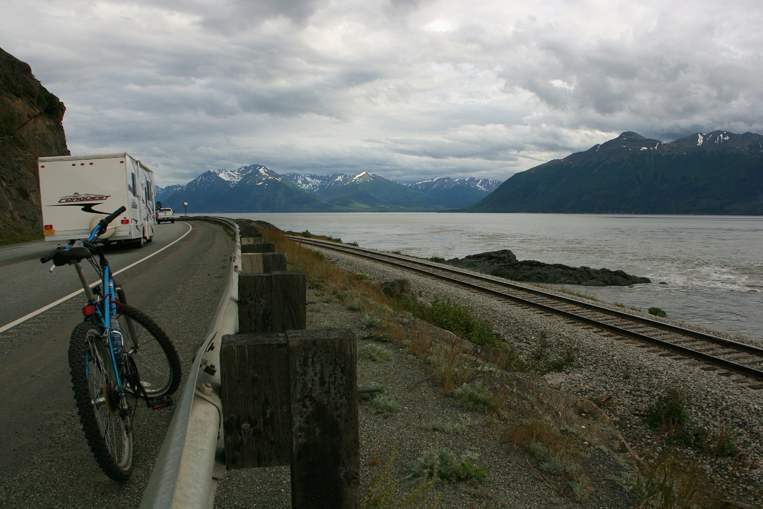 An RV passes a bicycle sitting on the Seward Highway near Alaska&#039;s Cook Inlet and Kenai Mountains.
