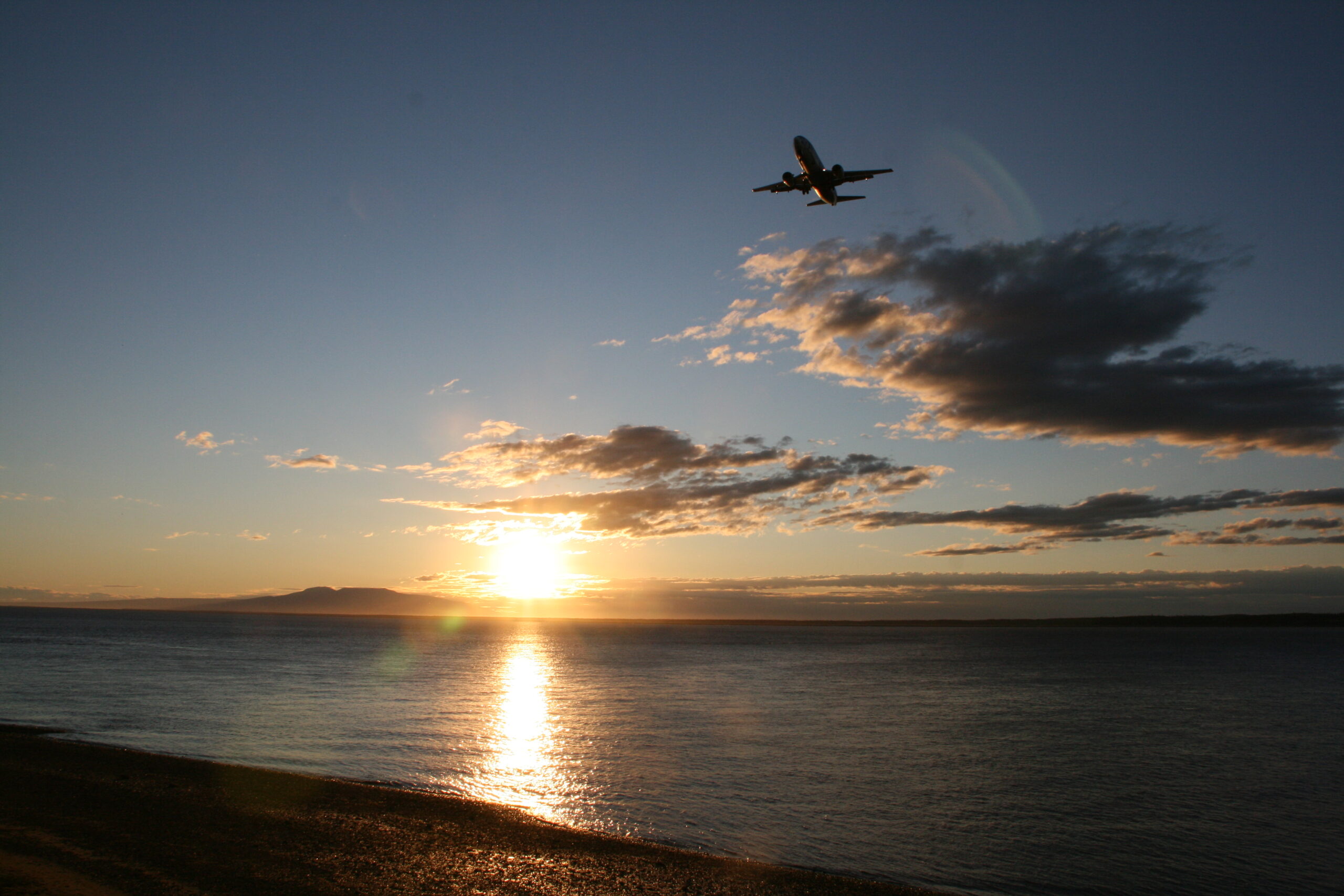 A plane flies over Point Woronzof as the sun sets near Anchorage's Coastal Trail.
