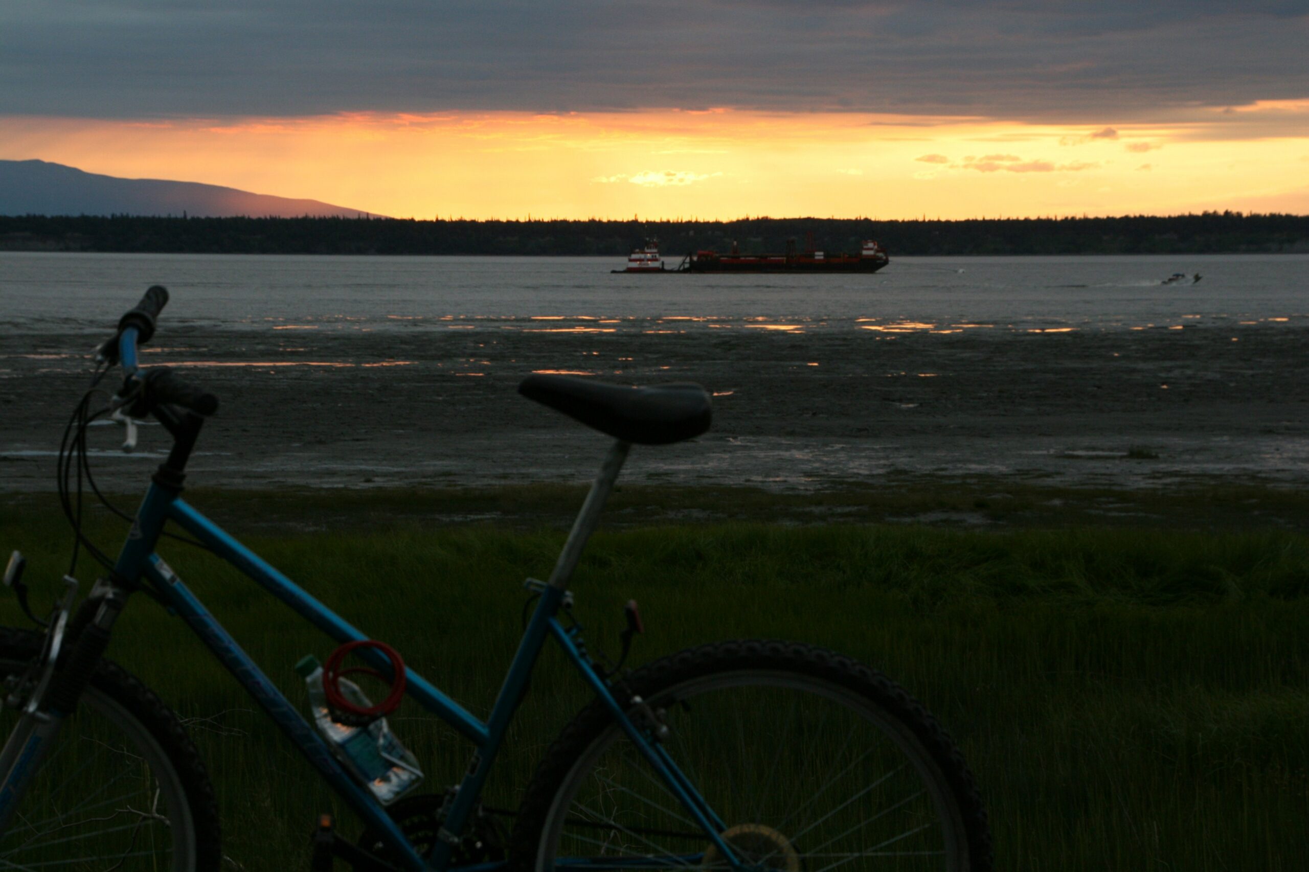 A bicycle sits on Anchorage's Coastal Trail as the sun sets over the Cook Inlet.