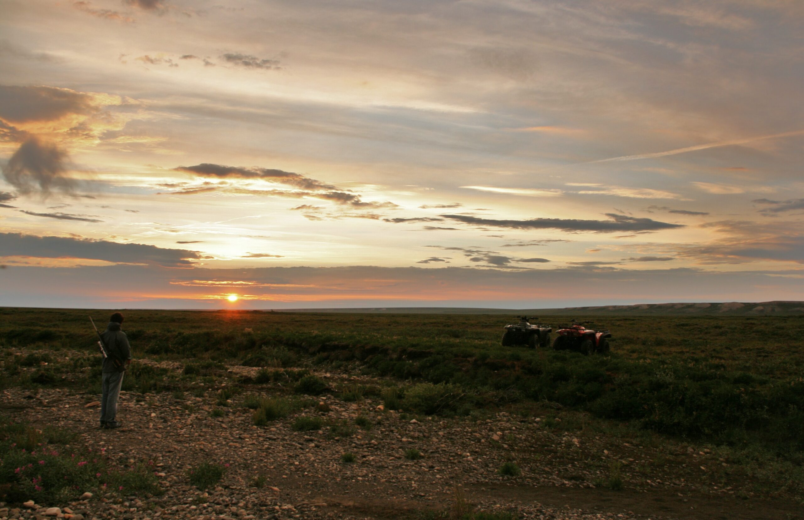 The sun dips toward the horizon above two ATVs.