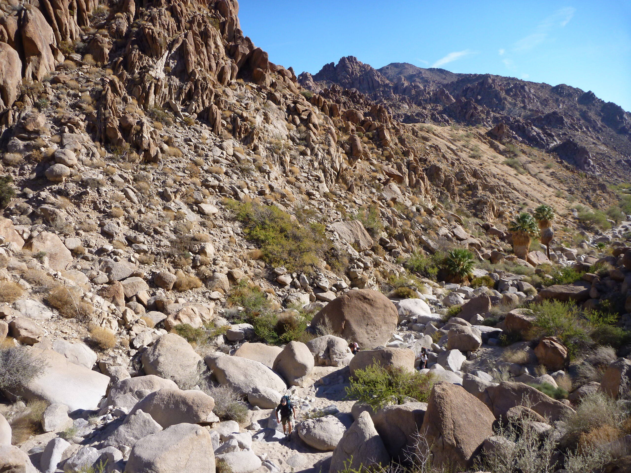 Hikers traverse boulders near Victory Palms Oasis.