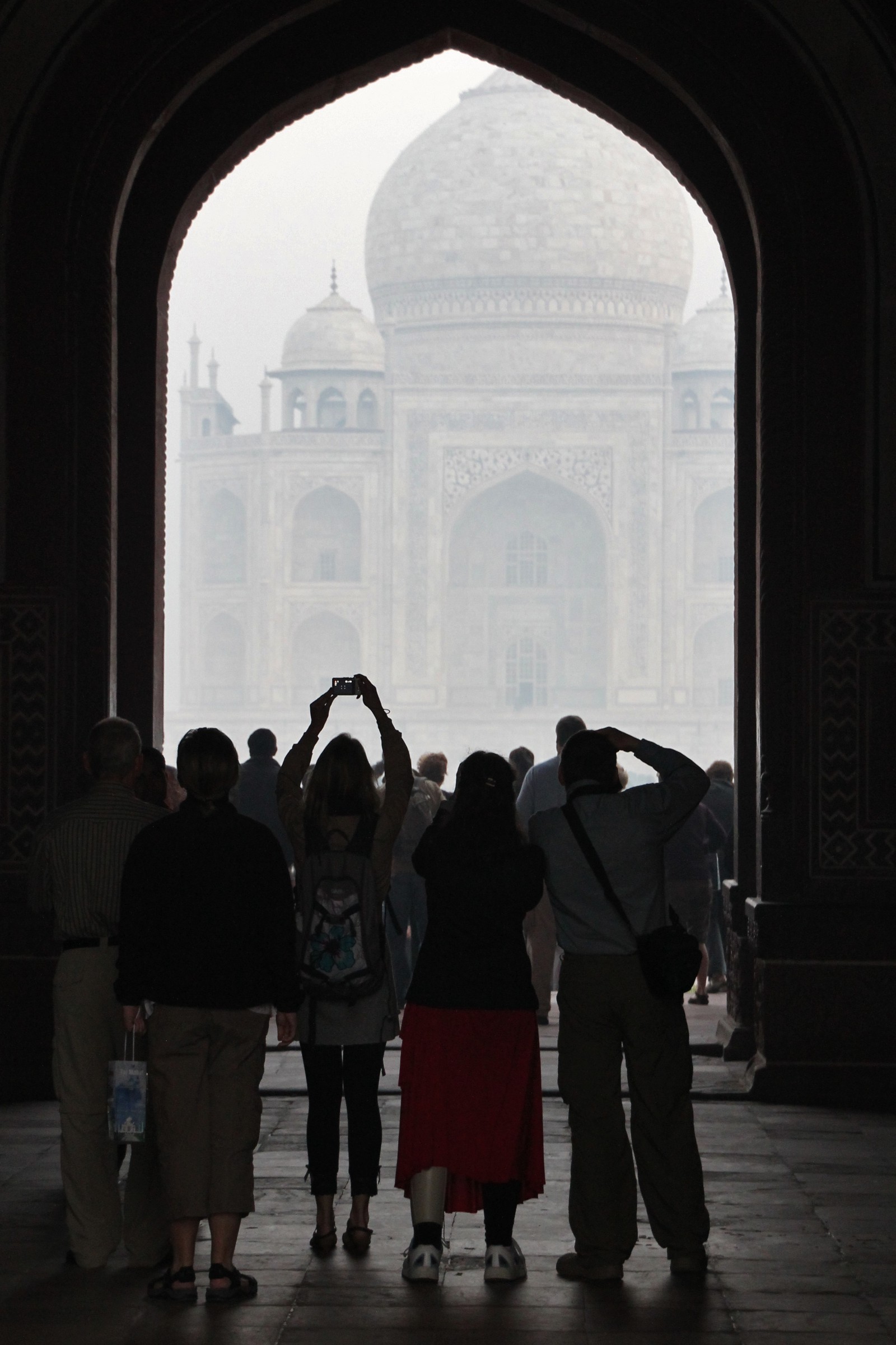 Tourists photograph the Taj Mahal through the complex's Great Gate at sunrise.