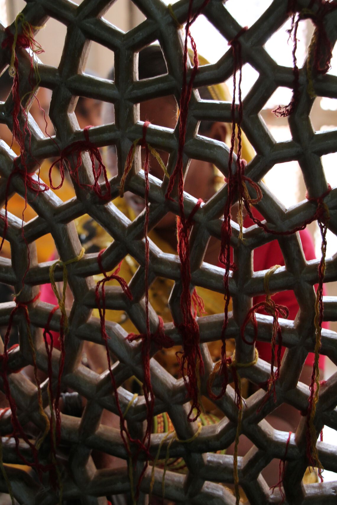 A woman makes a wish and ties thread to lattice in Saint Shaikh Salim Chishti's white marble tomb.