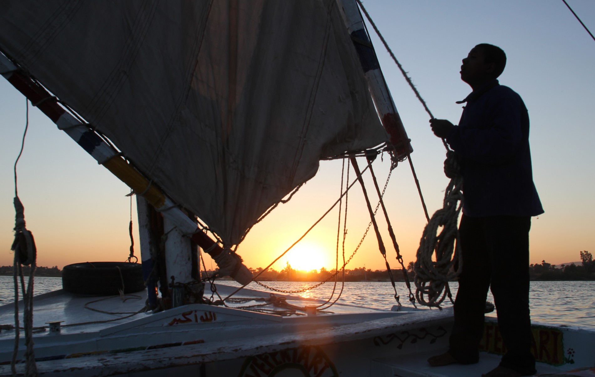 A felucca captain adjusts the sail on his boat on the Nile River at sunset.