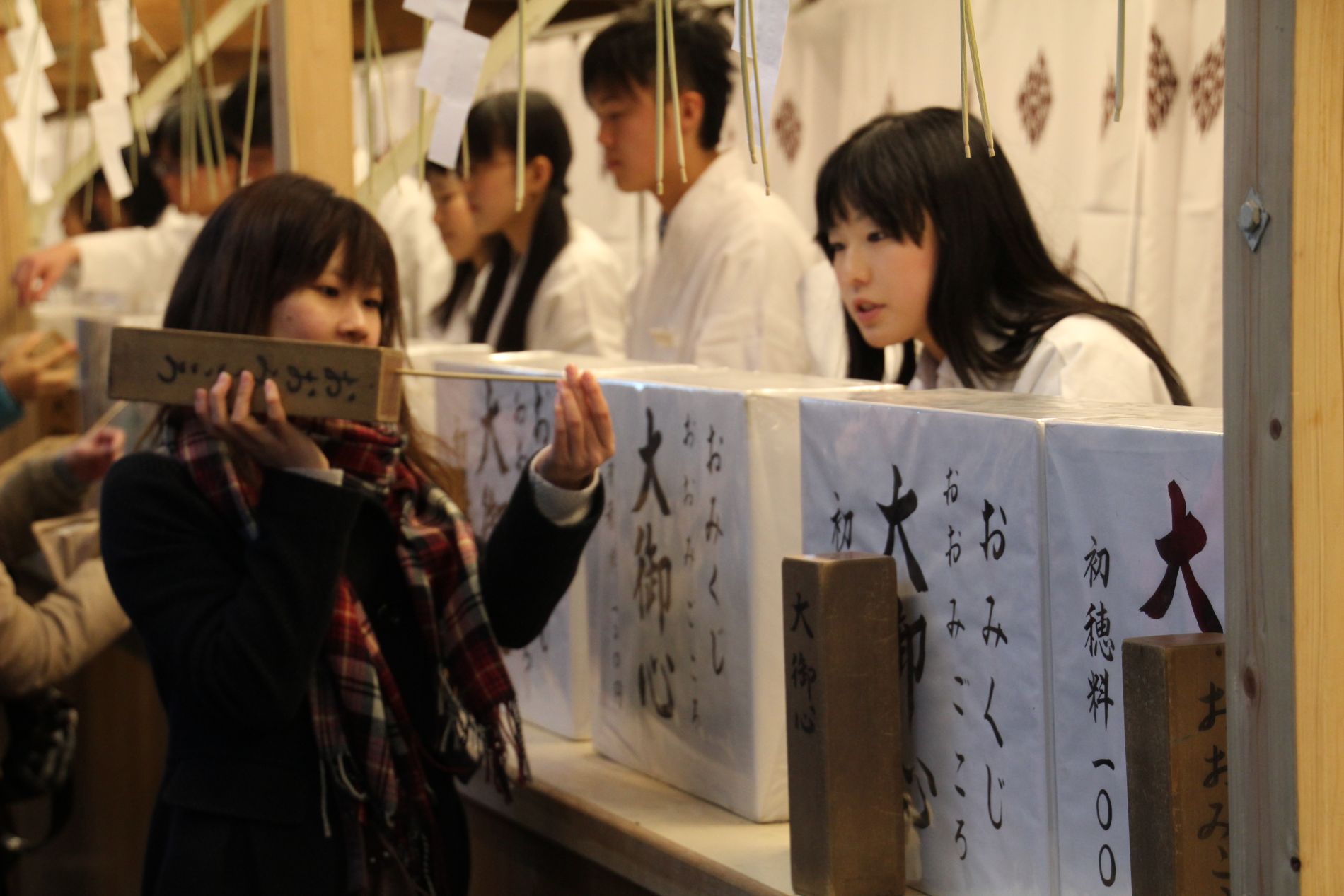 A woman uses a wooden box filled with random numbers to determine which omikuji she'll receive.