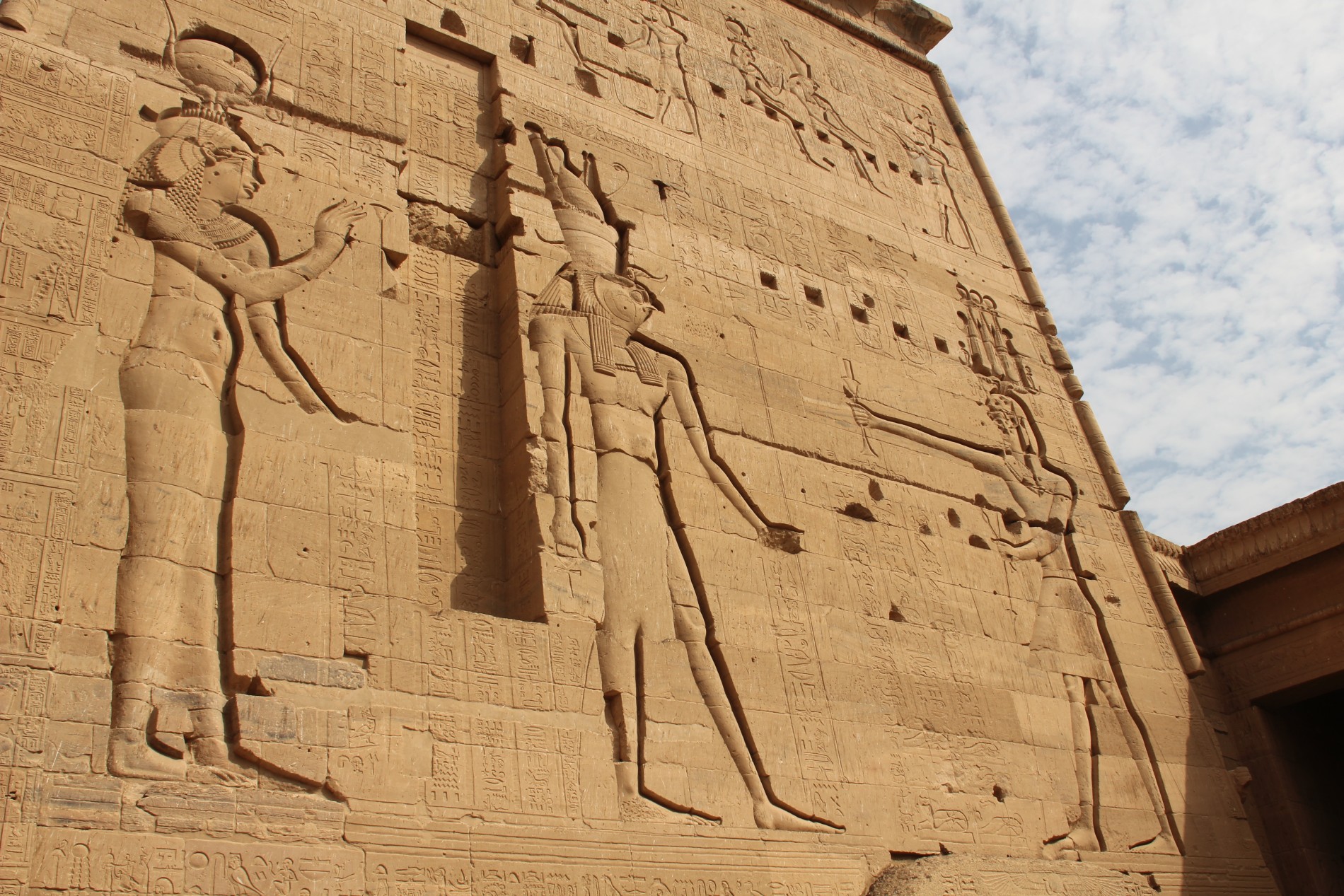 Carvings of Isis, Horus, and Osiris appear on the First Pylon of the Temple of Isis on Philae Island, Egypt.