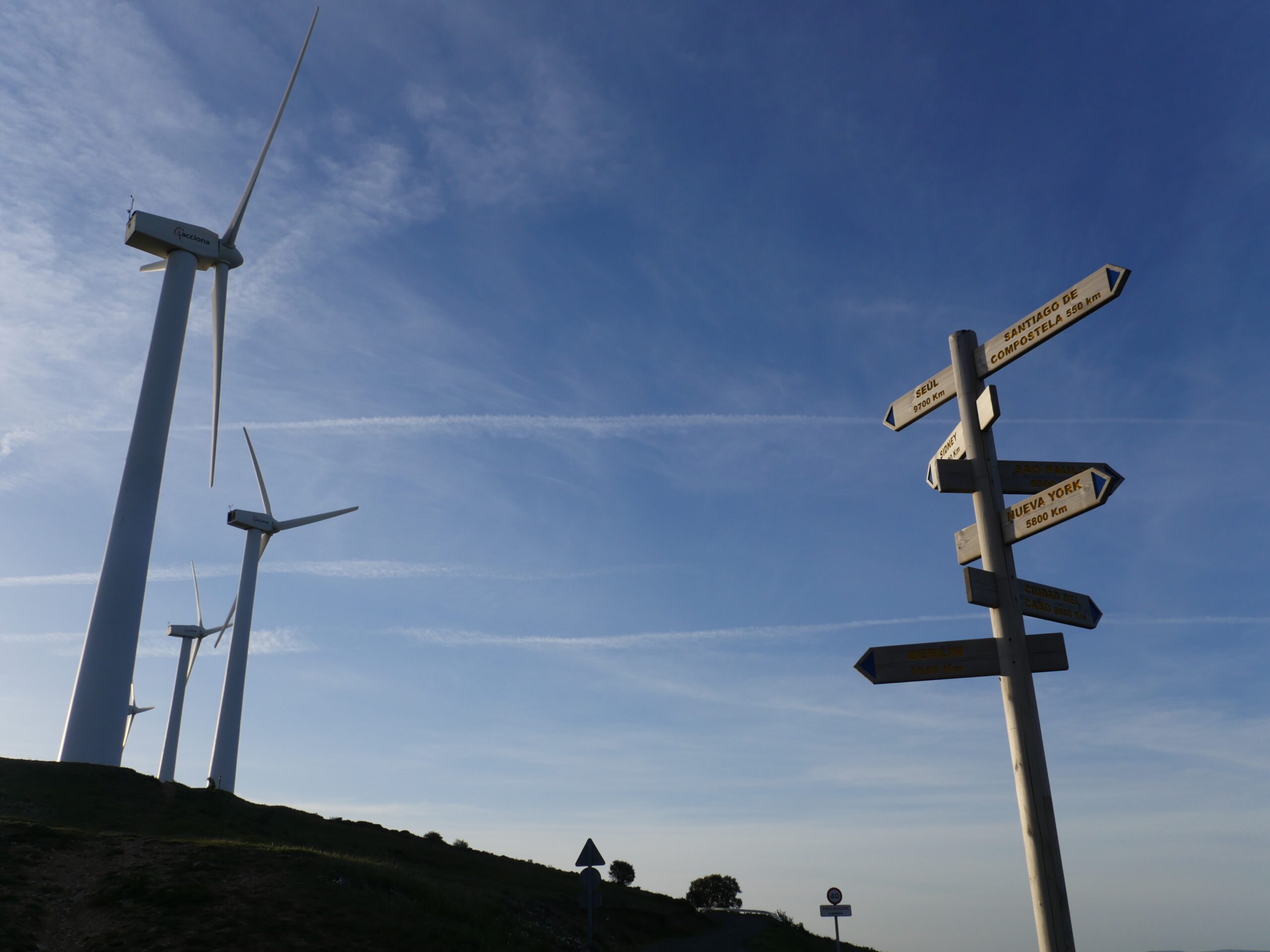 Signs point to the way to Santiago and other cities near windmills above Zariquiegui, Spain.