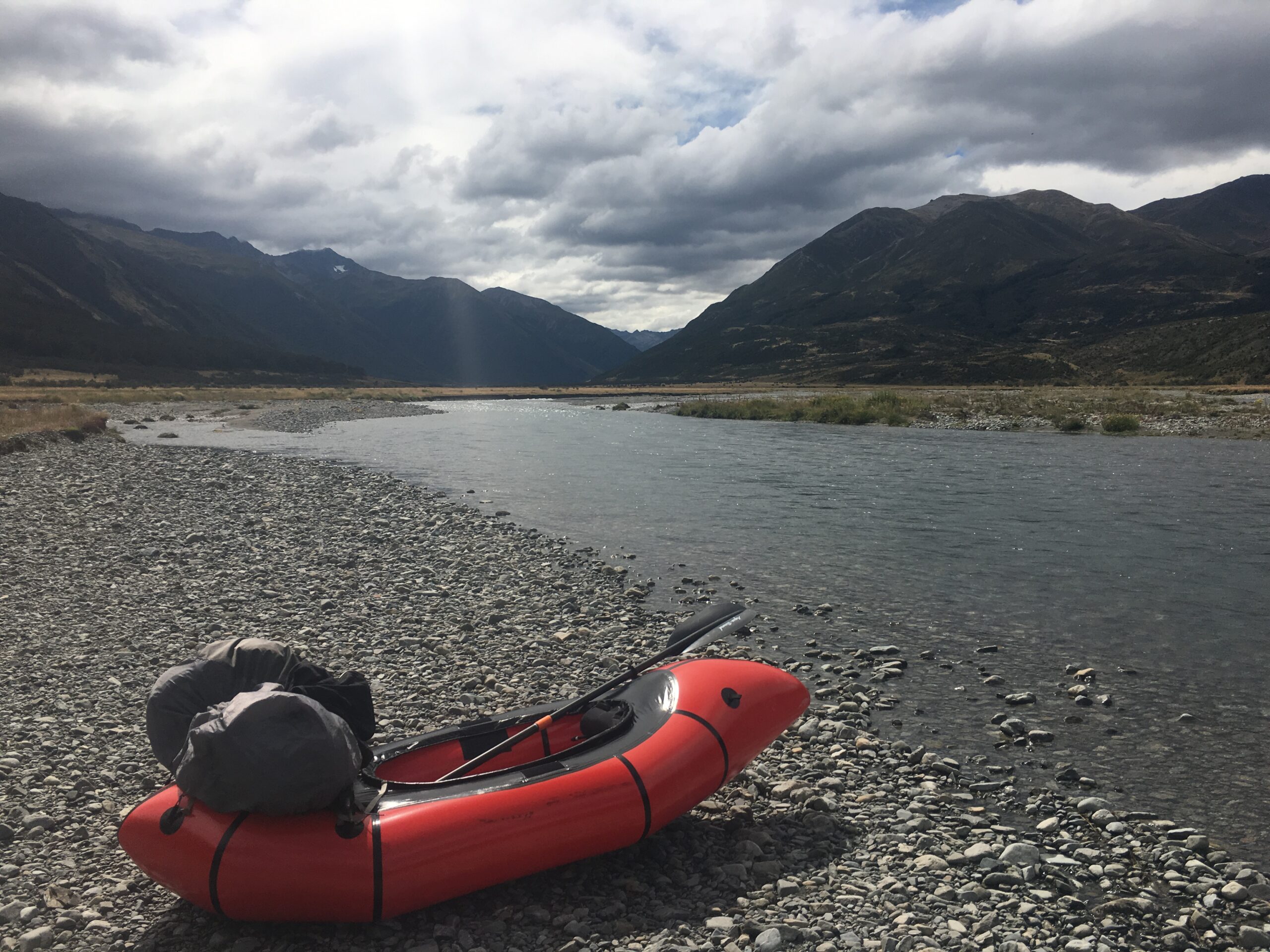 A packraft sits on the edge of the Waiau River, flanked by Mount Mahanga and the Saint James Range.