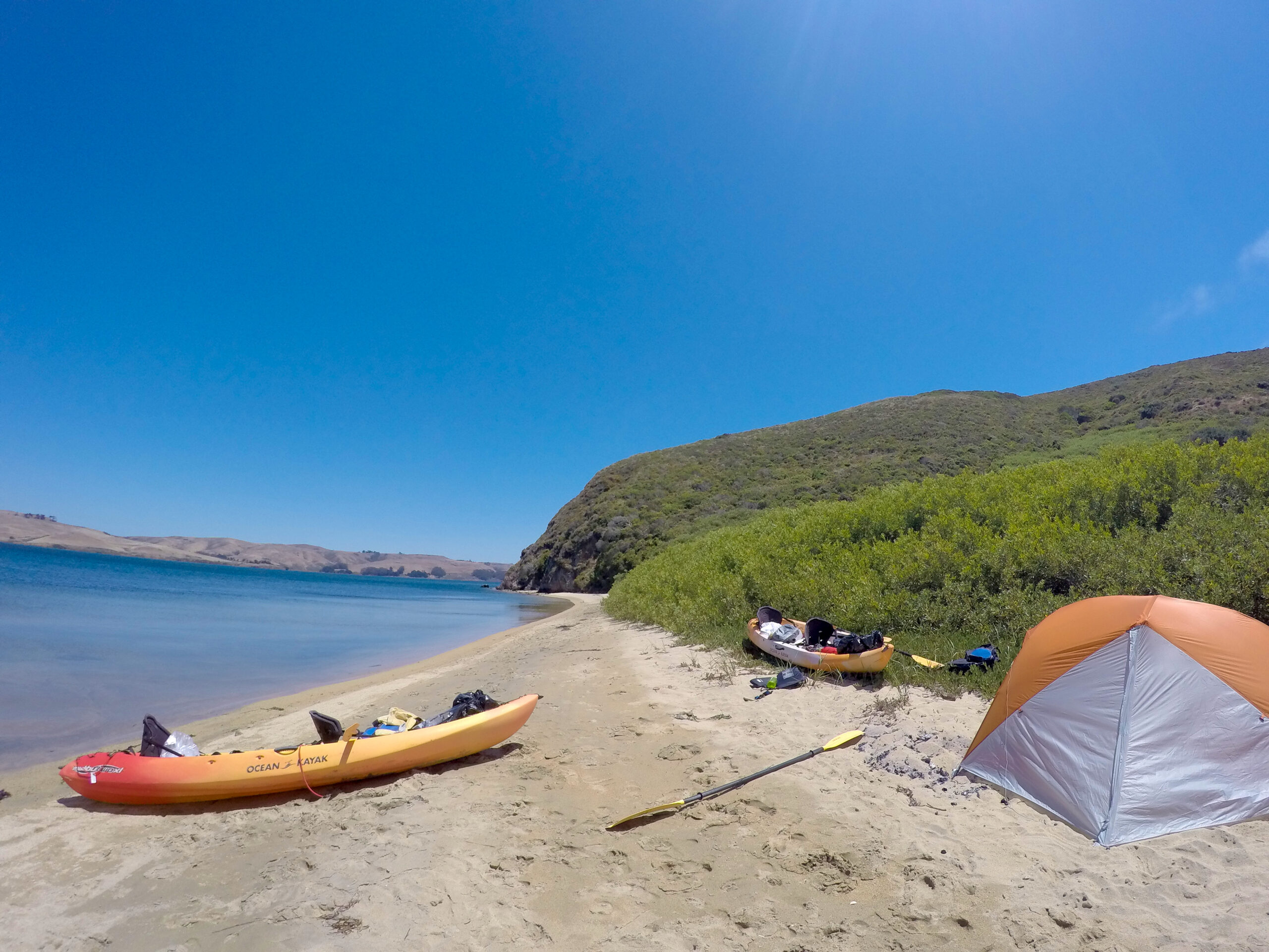 Kayaks and a tent sits sits on a beach in Tomales Bay, California.